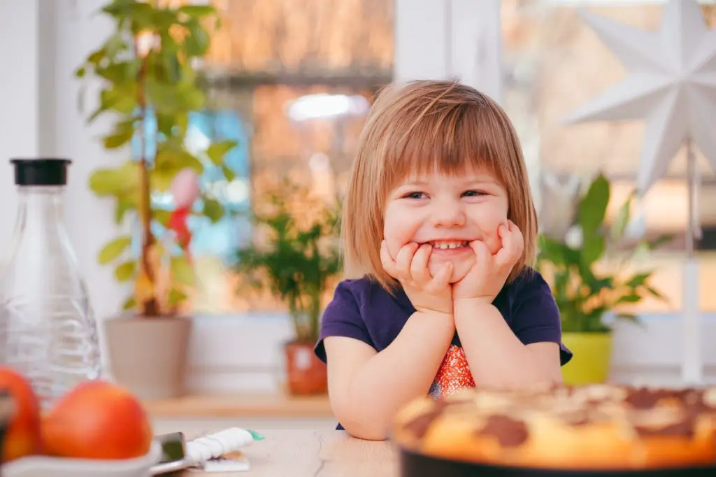 a girl smiling with a food in front of her - frugal living tips for moms in 2020